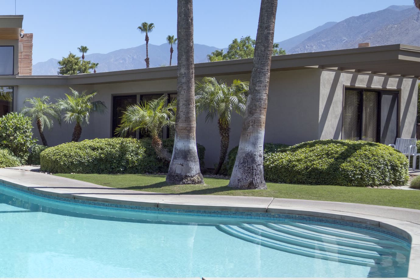 Inspiration photo: a low single-story wing with sliding glass doors, palms and lawn beside a pool