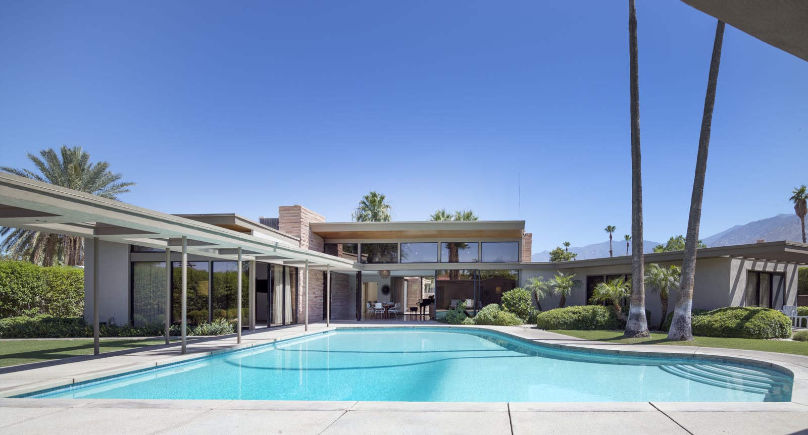 Inspiration photo: a mid-century house, a covered walkway and a single-story wing around one large pool and lawn under a clear sky