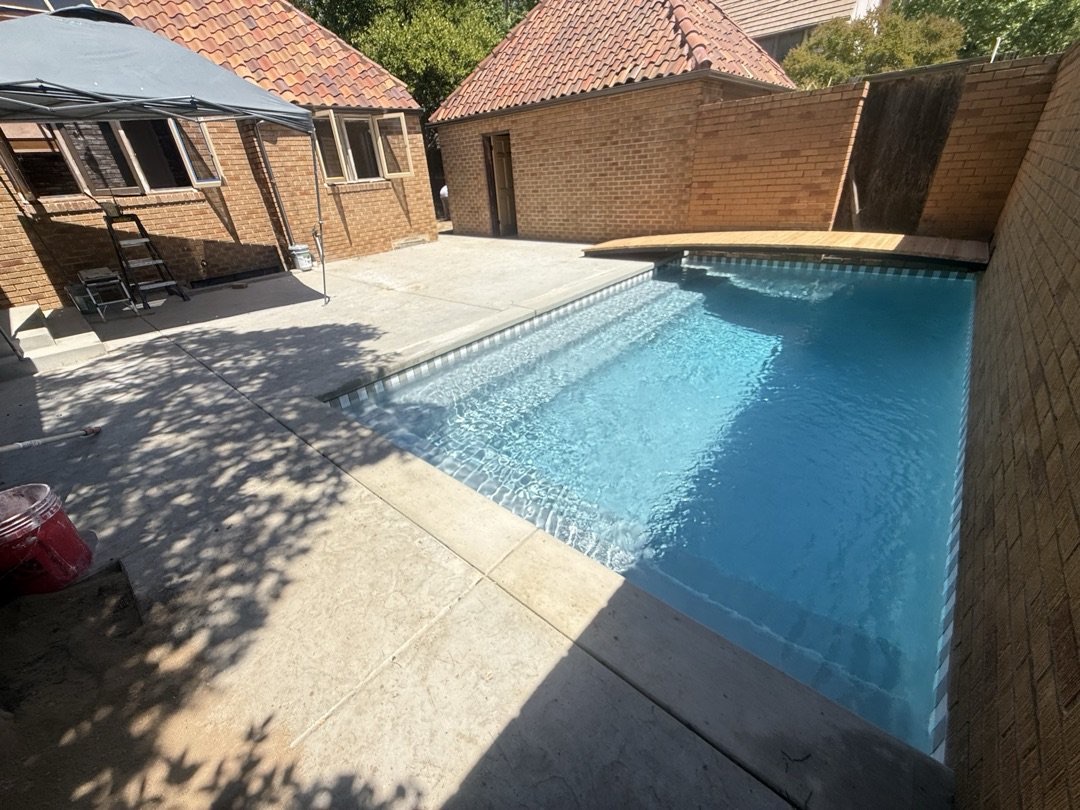 Rebuilt rectangular pool with bright blue water beside a brick house and new concrete deck