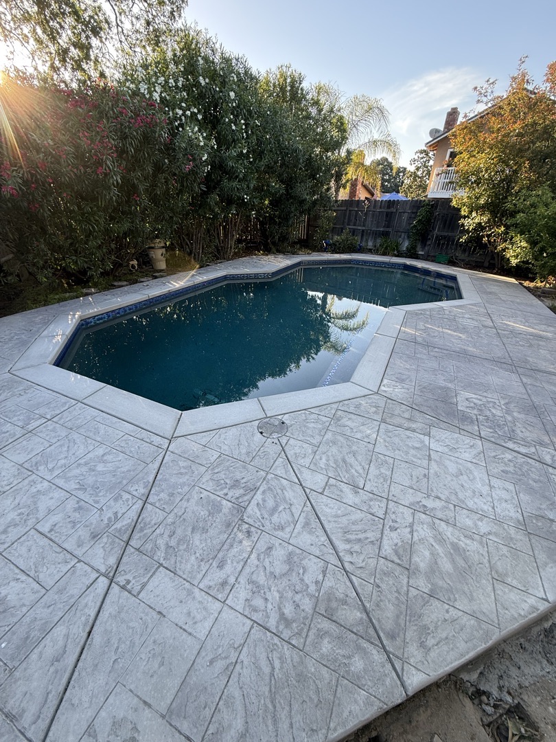Pool surrounded by a new pale stamped stone-pattern deck at sunset