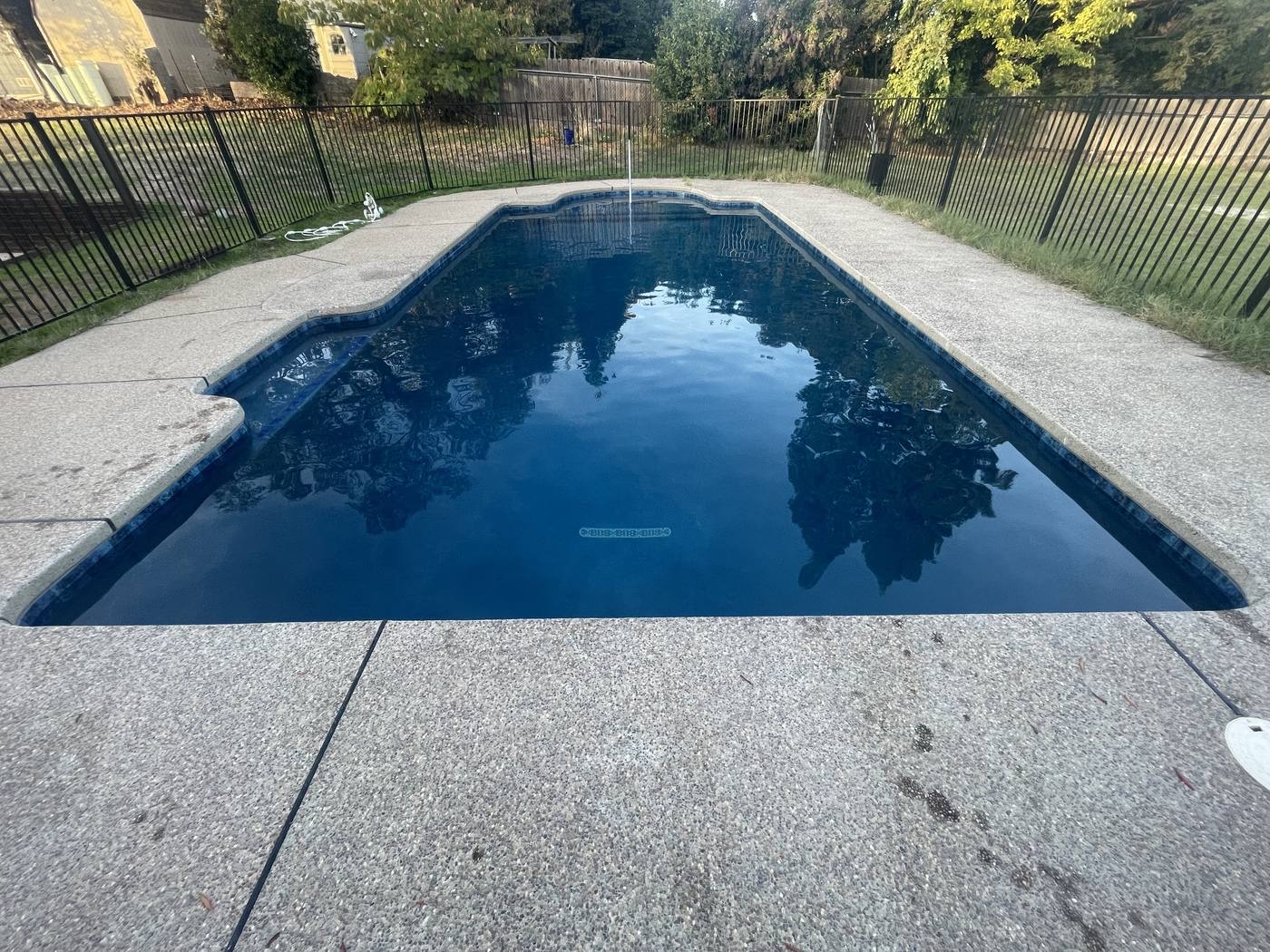Rectangular pool with dark blue finish reflecting trees, behind a black fence