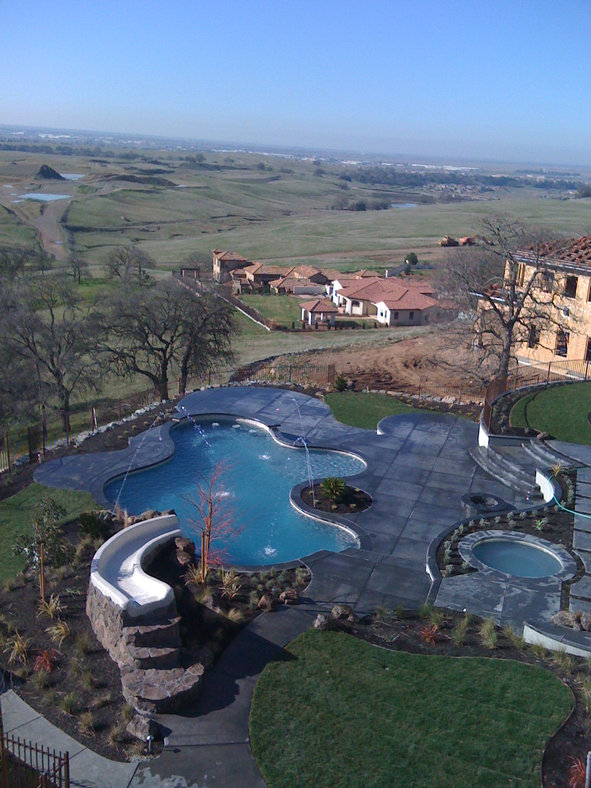 Hillside backyard with a free-form pool, a rock slide, a round spa and a stamped concrete deck above open valley views